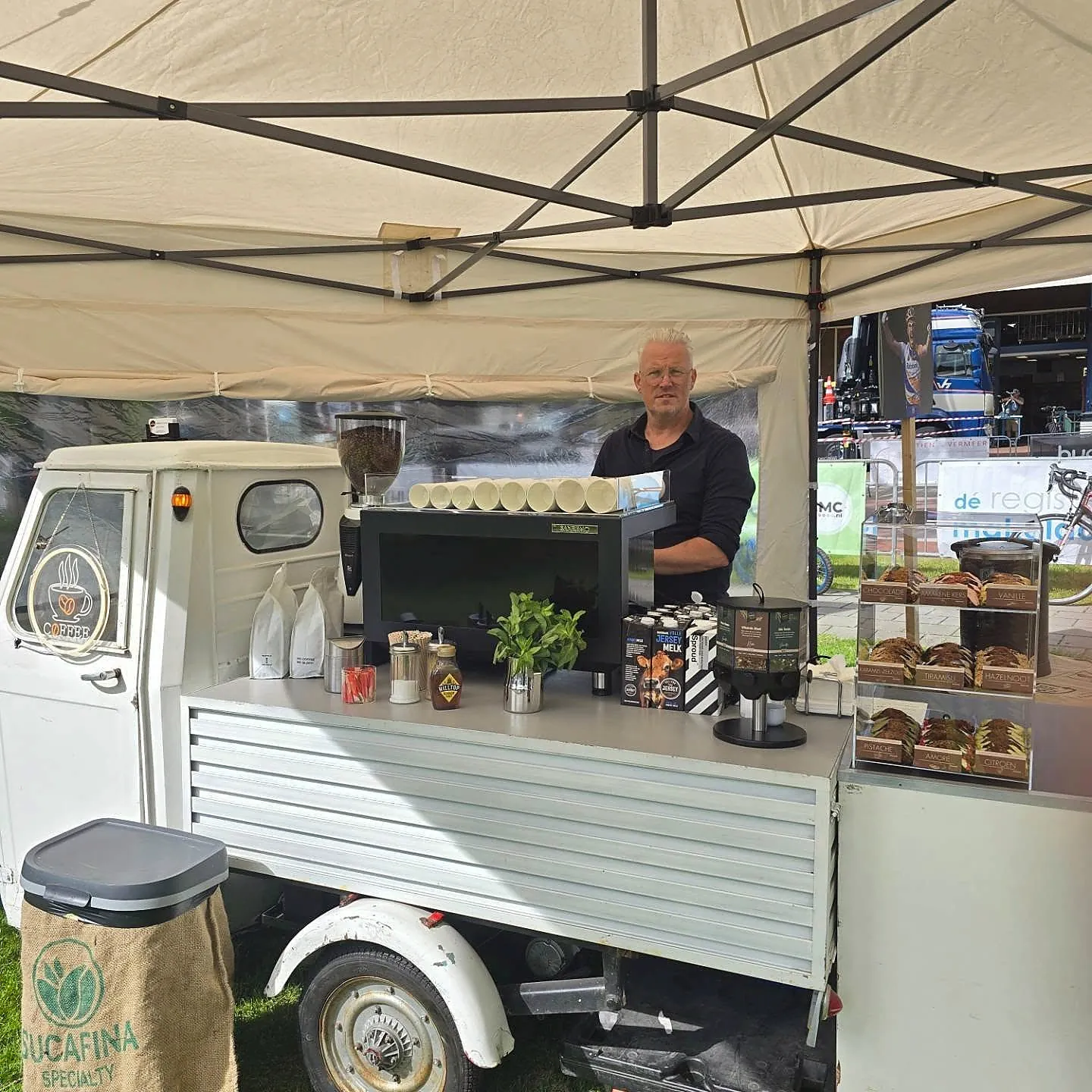 Jeroen achter zijn mobiele koffietuktuk tijdens een evenement, met espressomachine en lekkernijen