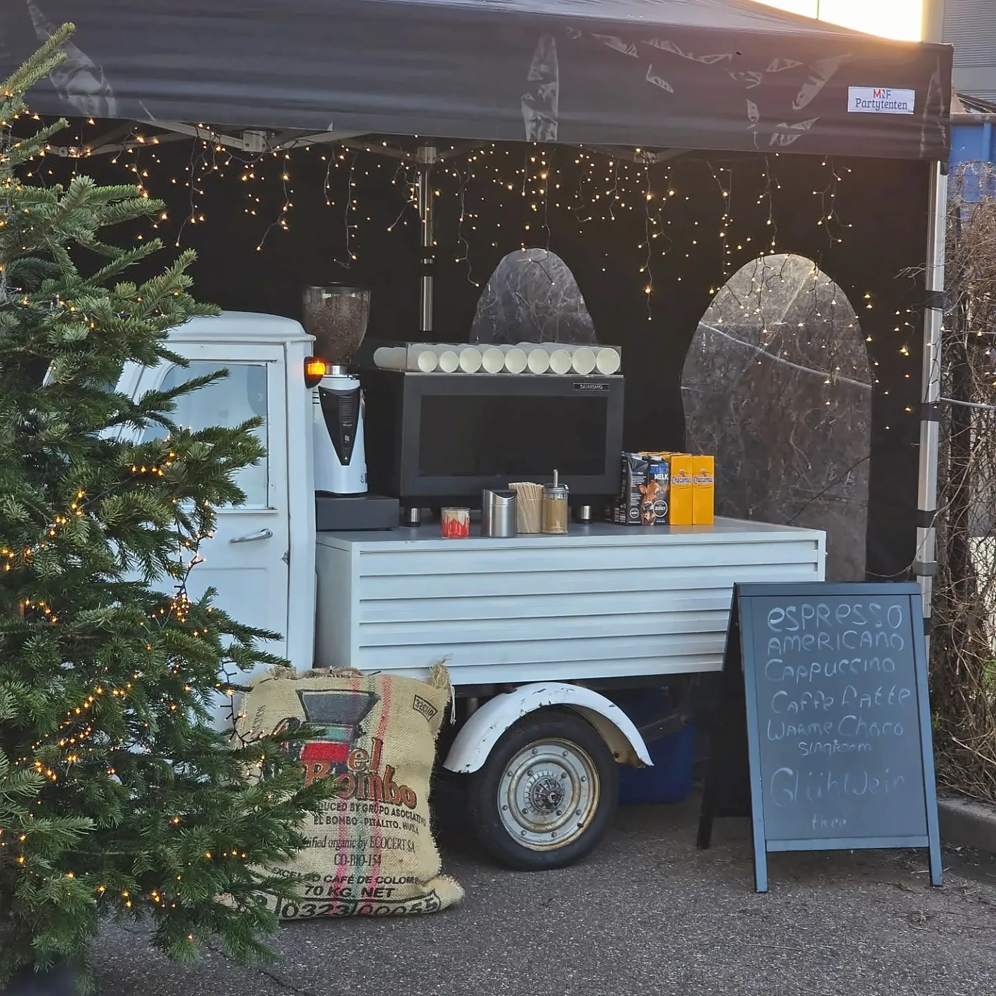 De mobiele koffiebar onder kerstverlichting, met een krijtbord met de kaart